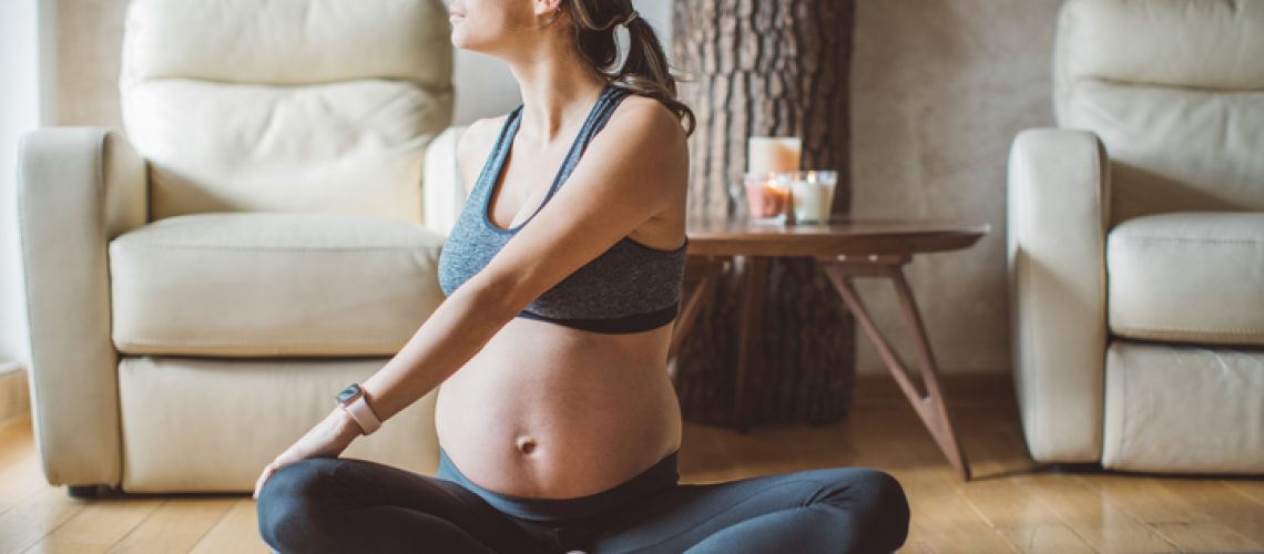 Young pregnant woman exercising at home. She workout on exercise mat and stretching.